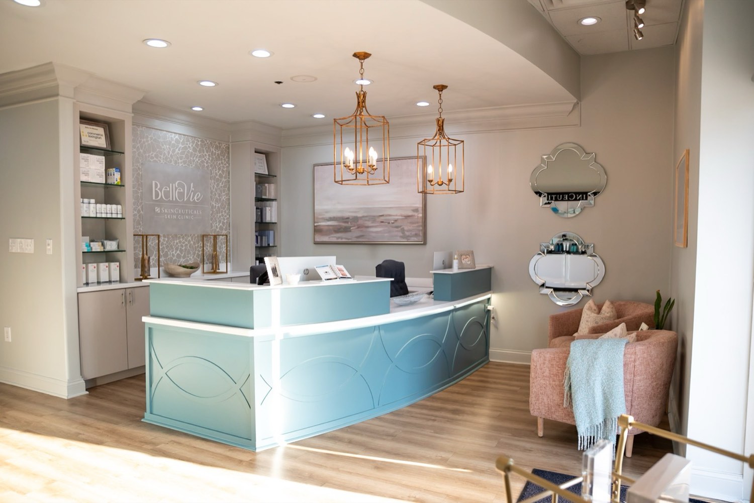The Belle Vie reception: a curved seafoam desk, brass lantern pendants, oak floors and a SkinCeuticals Skin Clinic wall sign.